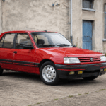 Red Peugeot 309 GTI parked outside a period industrial building